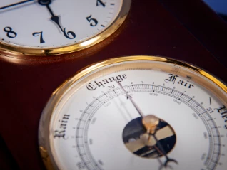 Close-up: Vintage wood/brass weather station shows a barometer face with 'Change, Rain, Fair' below a clock...
