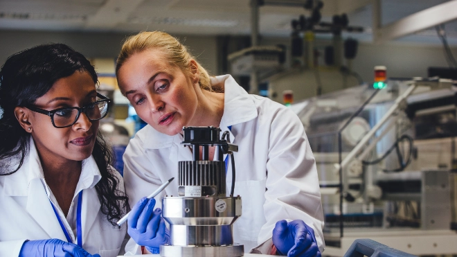 Two female lab workers in white coats and gloves