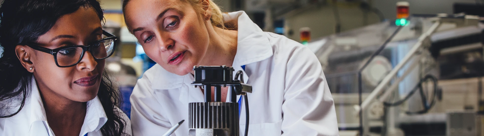 Two female lab workers in white coats and gloves